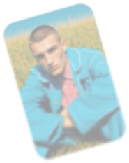 Blurred photo of a young man wearing a blue jacket sitting outdoors with greenery in the background.